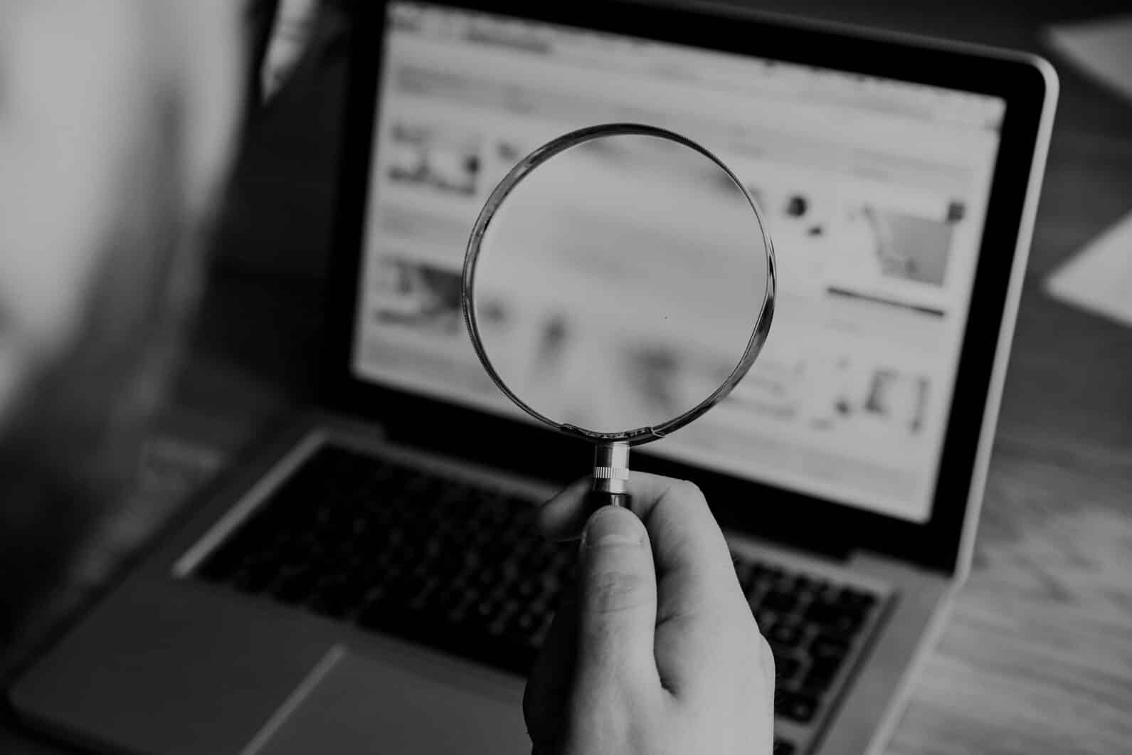Magnifying glass over a laptop screen, illustrating the background check of a Chinese supplier